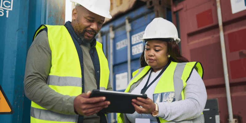 Alt text: Two supply chain managers review inventory reports at a shipping port