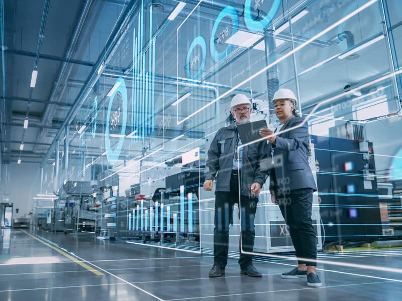 Two colleagues in factory viewing virtual overlay with graphs